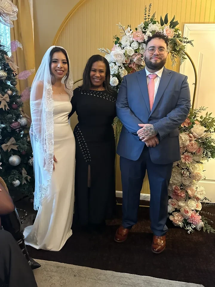 Couple with officiant under a floral arch at an indoor ceremony