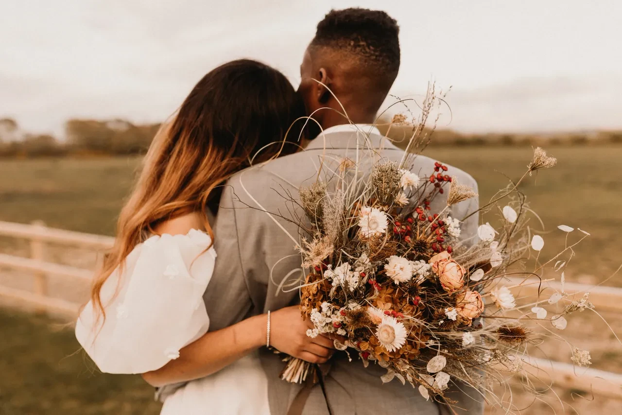 Couple embracing in a field holding a wildflower bouquet