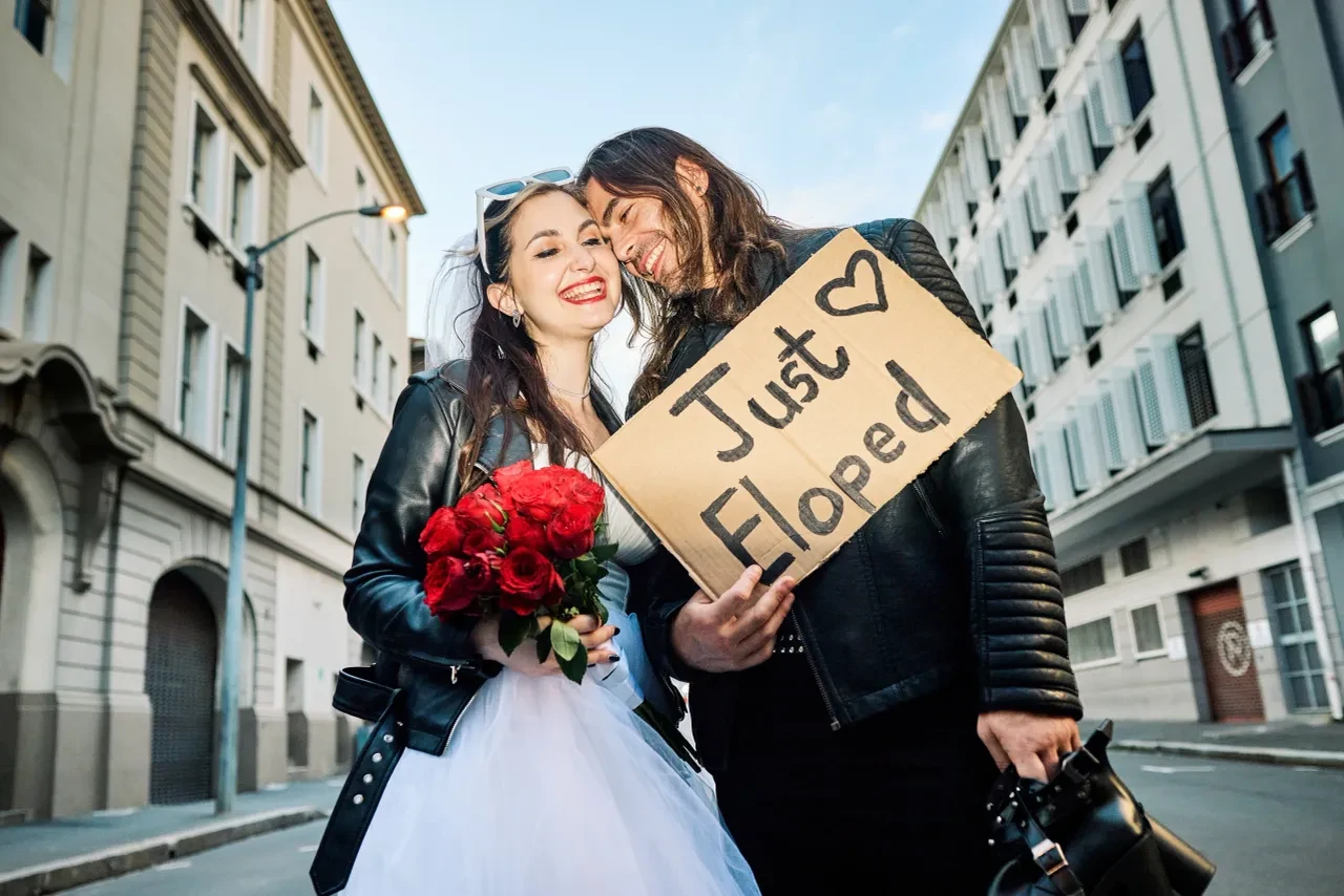 Joyful couple on a city street holding a Just Eloped sign