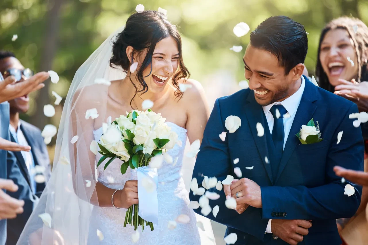 Bride and groom laughing as guests shower them with petals