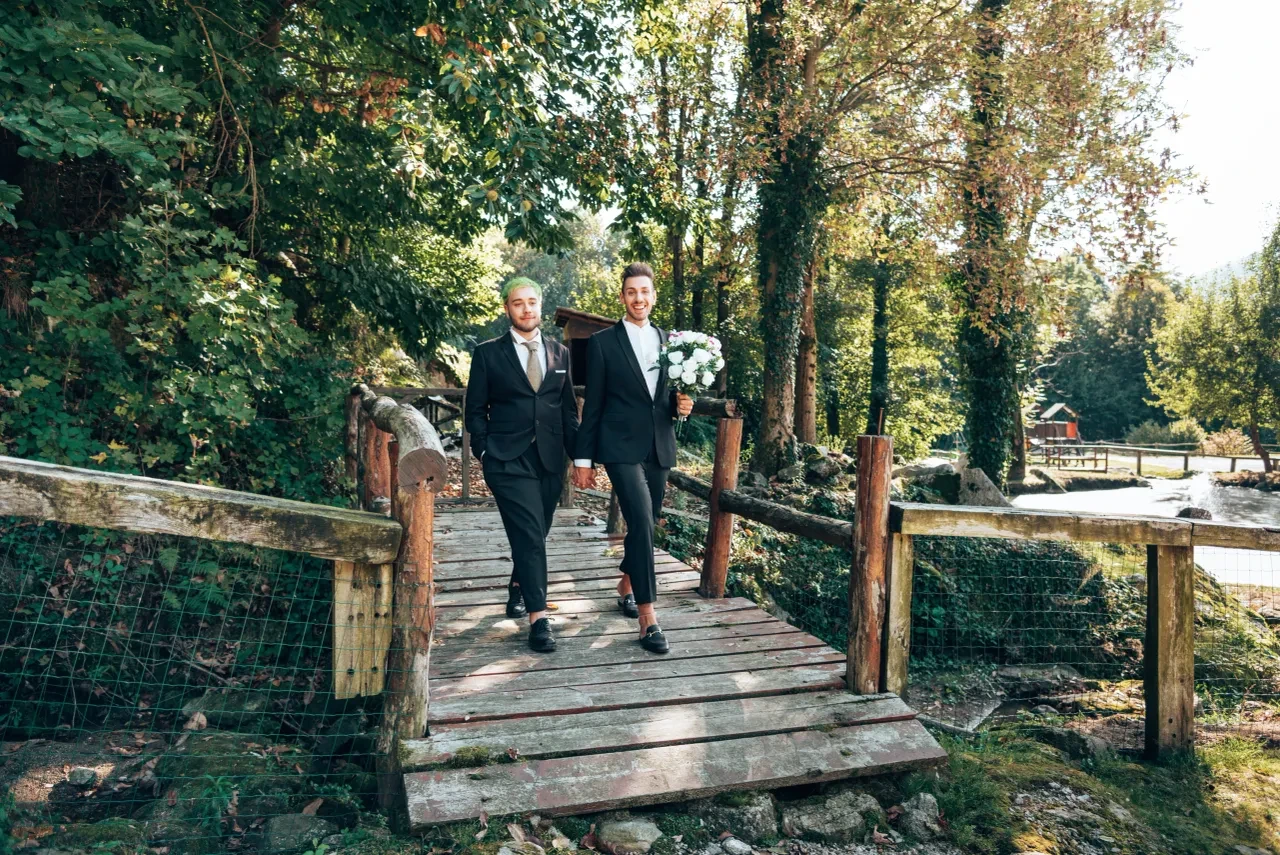 Two grooms walking across a wooden bridge in a forest
